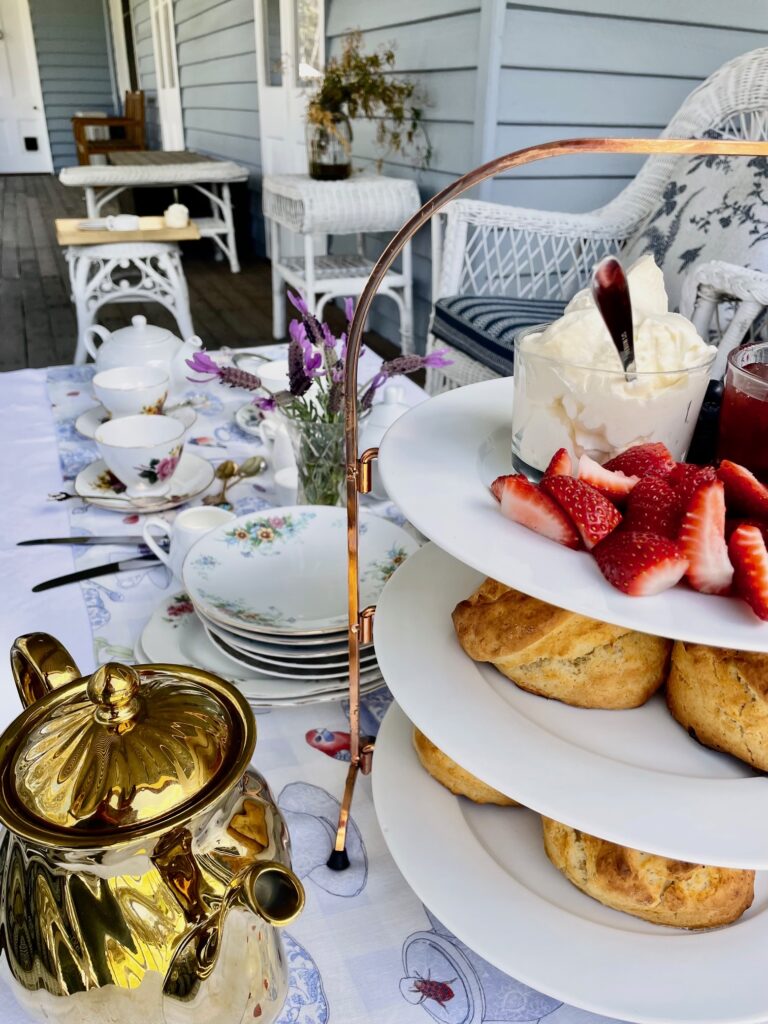 tea service, tiered tray with scones, jam and cream all placed on a table on verandah