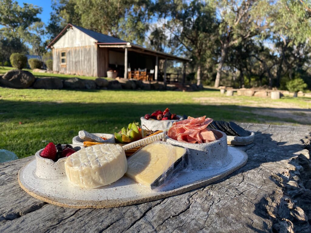 Platter loaded with fruit, cheeses, charcuterie with lawn and historic timber building in background