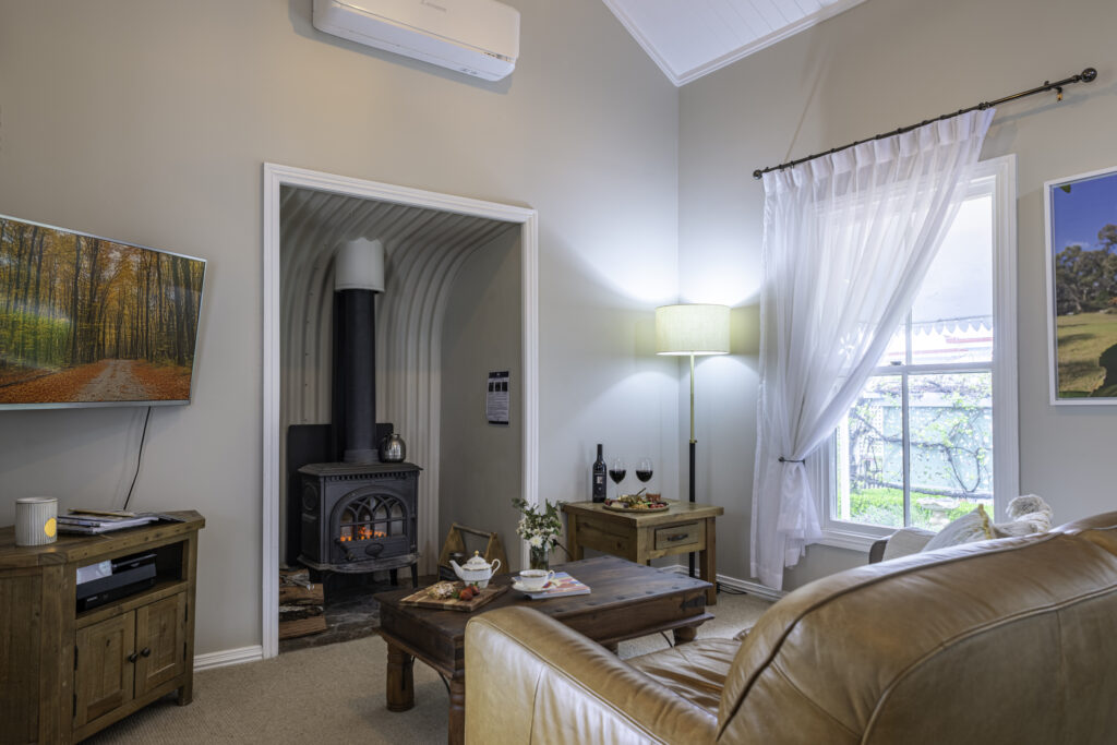 Living area of Camelia Cottage, light filled relaxing room with lounge, fireplace, TV, airconditioning